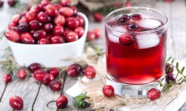 A bowl of cranberries and a glass of cranberry juice
