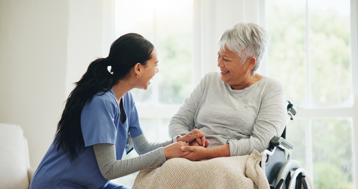 Woman in scrubs smiling at woman in wheelchair
