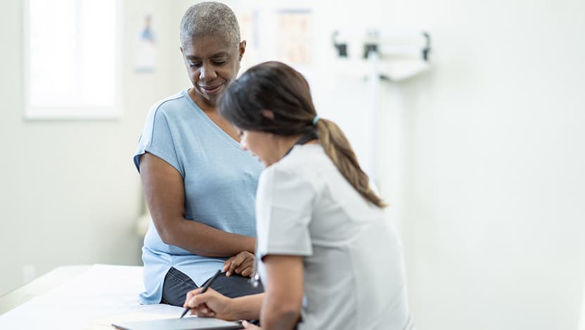 A woman sitting on an exam table consults with a doctor.