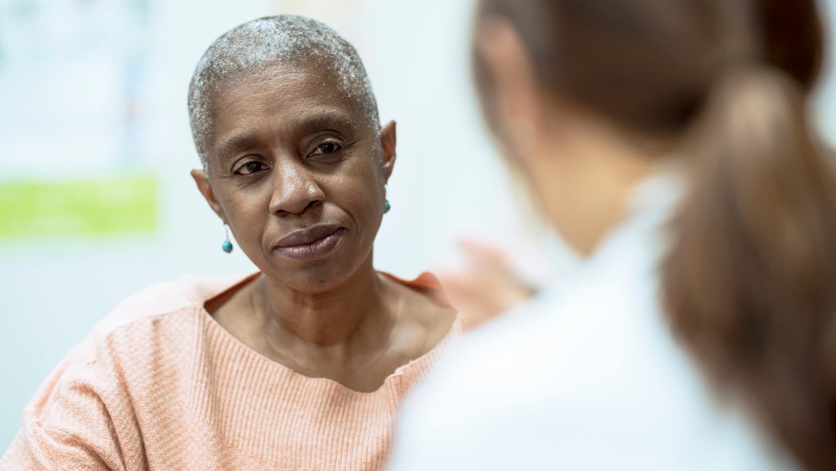 Older Black woman with serious expression facing physician in white coat