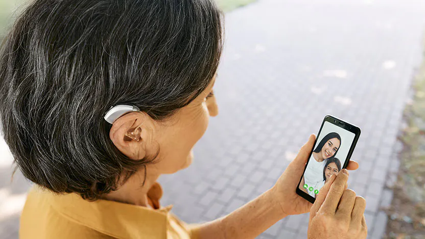 Senior woman with a hearing aid behind the ear communicates with her daughter and granddaughter via video communication via a smartphone.