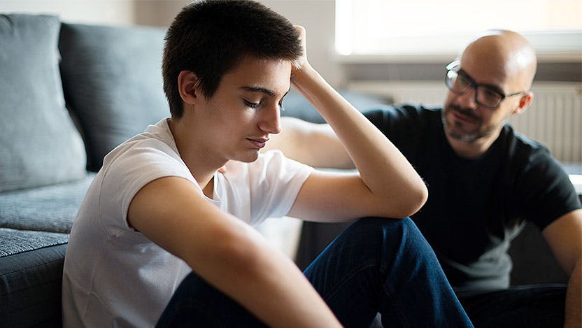A teenager looking somber while talking with their parent