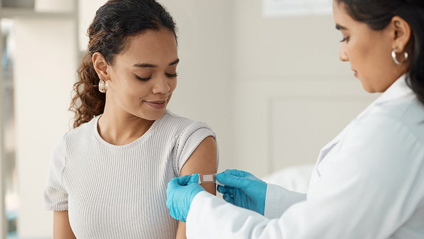 Health provider putting a bandaid on a woman's arm after a vaccine