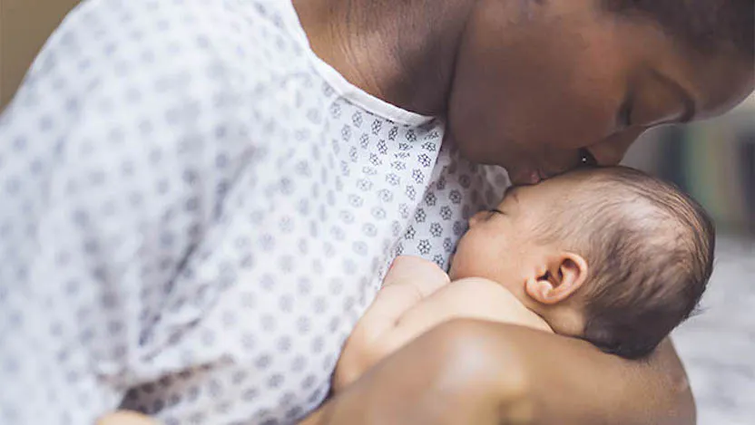 Mother in medical gown kissing newborn baby on forehead