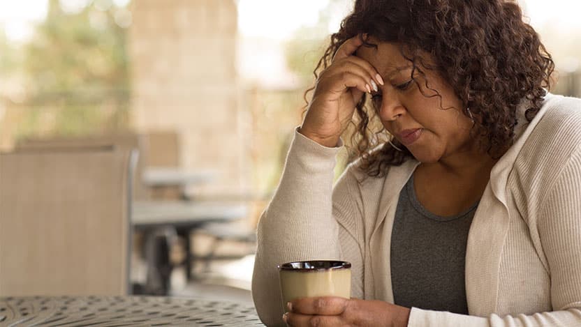 Woman with hand on her forehead while having coffee