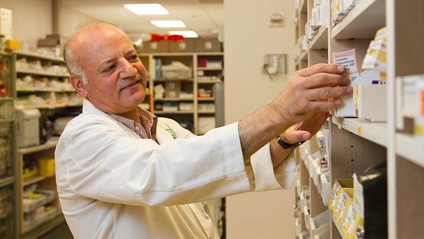A pharmacist selects a drug from a display case. A UChicago pharmacologist sees traction in push to lower cancer drug costs.