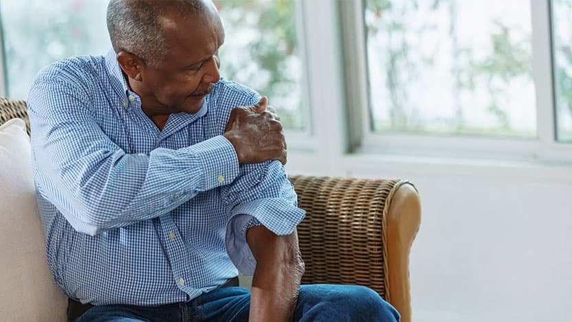 Man sitting at home, rubbing sore shoulder