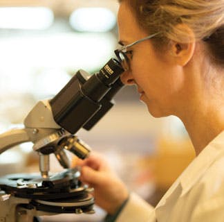 Female cancer researcher looking in microscope