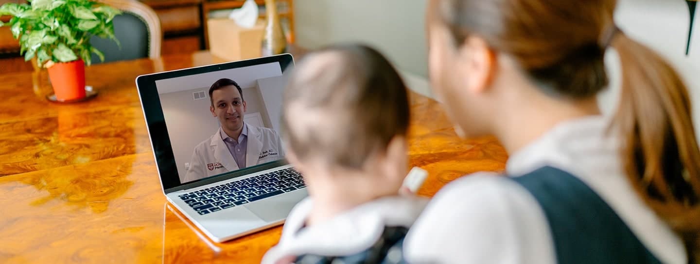 Woman holding her baby looking at a doctor on her computer screen