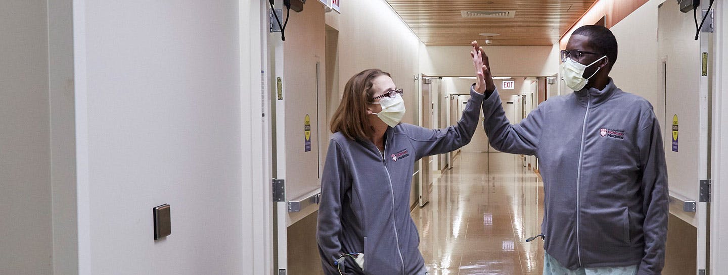 Triple-organ transplant patients, Sarah McPharlin and Daru Smith, high-five each other in the hospital.
