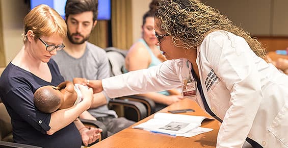 Prenatal nurse instructor Evelyn Turner guides a pregnant mom cradling a doll during an infant care class