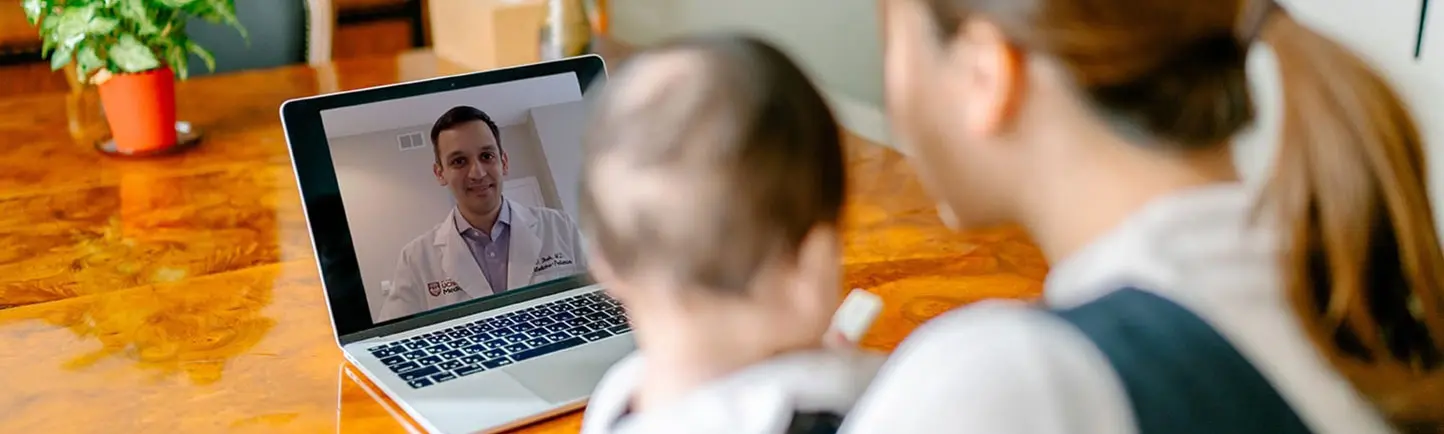 Patient holding baby looking at video visit with a doctor on her computer screen